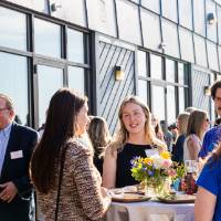 Group of 5 young event attendees standing around table outside, enjoying conversation
